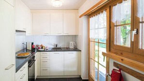 A modern kitchen with white cabinets, a black countertop, a stove, and a window with a view of greenery. - Ferienhaus Muntschi, (Andeer), by Interhome (Andeer)