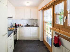 Eine moderne Küche mit weißen Schränken, einer schwarzen Arbeitsplatte, einem Herd und einem Fenster mit Blick auf Grünflächen.