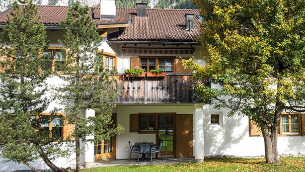 A multi-story building with a balcony, a dining area with a table and chairs, and a mountain backdrop. - Ferienhaus Muntschi, (Andeer), by Interhome (Andeer)