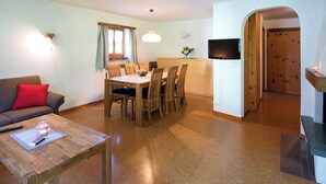 A compact living space with a dining area, a sofa, a coffee table, a TV, and a wooden door. - Ferienhaus Muntschi, (Andeer), by Interhome (Andeer)