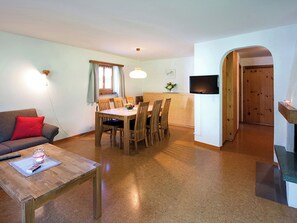 Ein gemütlicher Wohnbereich mit Essplatz, einer Couch, einem Couchtisch, einem Fernseher und einer Holztür.