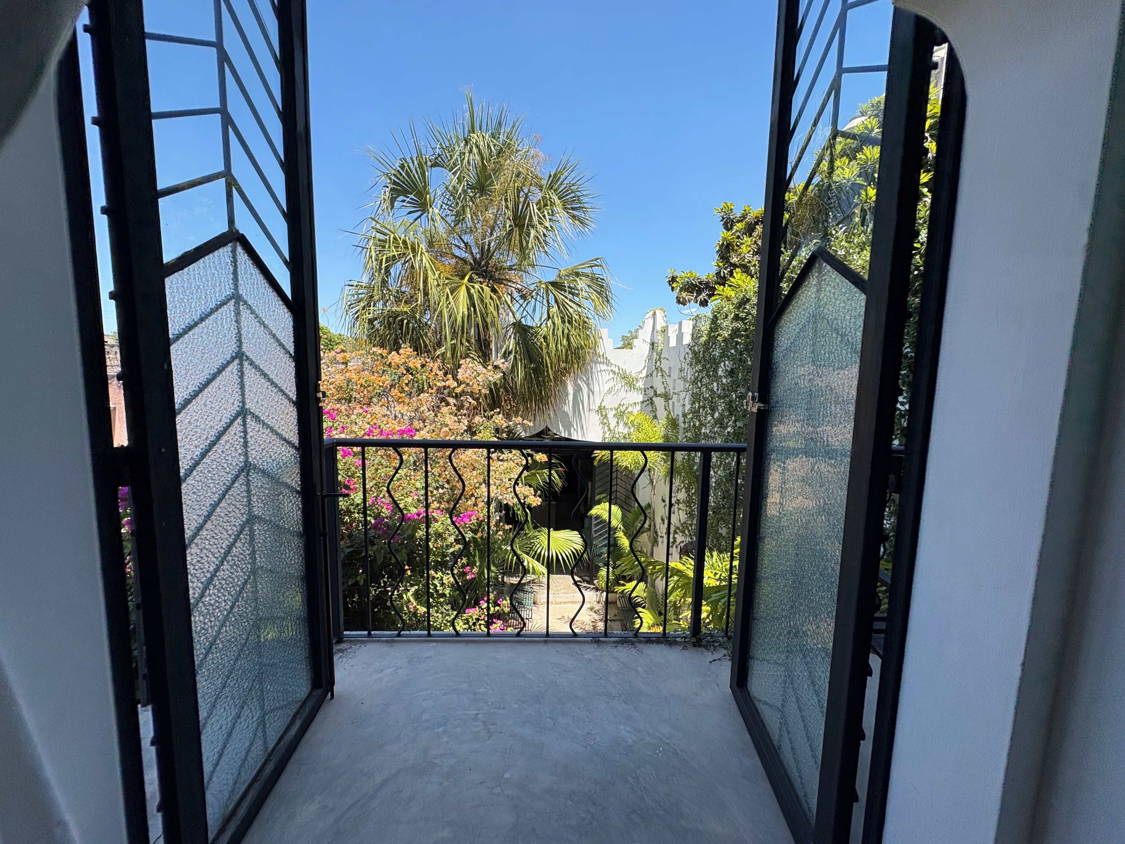 A balcony with a view of a garden, including palm trees and flowering plants.