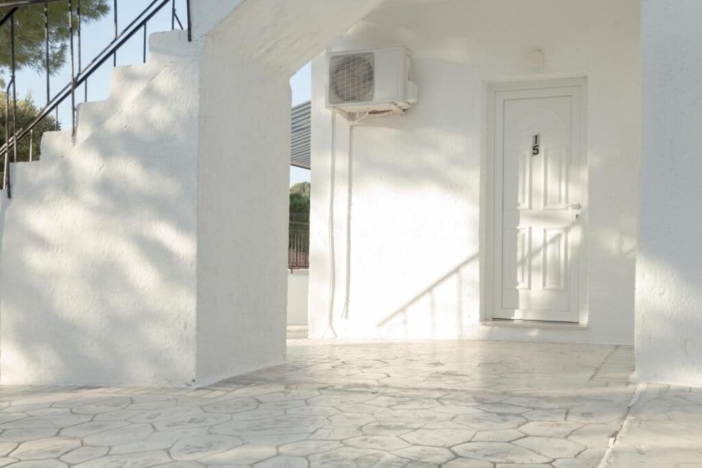 A white building with a tiled floor, a door with a number, and an air conditioning unit.