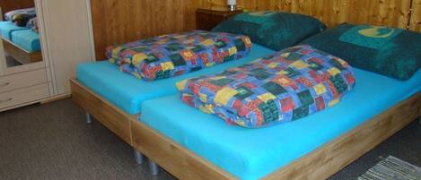 A double bed with blue bedding and colorful pillows in a room with wooden walls and a mirror.