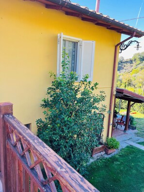 A yellow building with a wooden staircase, a window with white shutters, and a garden area with a bench and potted plants. - Farfa nature farmhouse with BBQ, Ping Pong and Fields for walkers (Castelnuovo di Farfa)