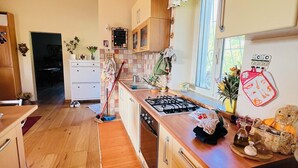 Una cocina con armarios de madera, una estufa a gas, un fregadero y una ventana con cortinas florales.