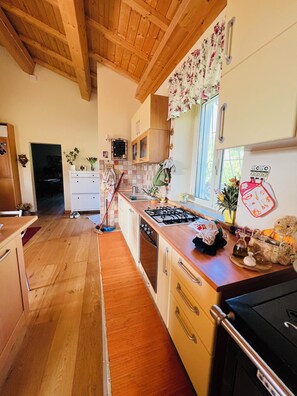 A kitchen with wooden cabinets, a gas stove, a sink, and a window with floral curtains. - Farfa nature farmhouse with BBQ, Ping Pong and Fields for walkers (Castelnuovo di Farfa)