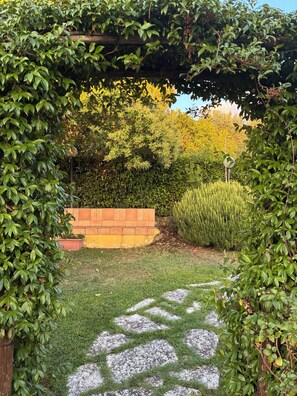 A garden pathway with a brick wall, greenery, and a pergola structure. - Farfa nature farmhouse with BBQ, Ping Pong and Fields for walkers (Castelnuovo di Farfa)