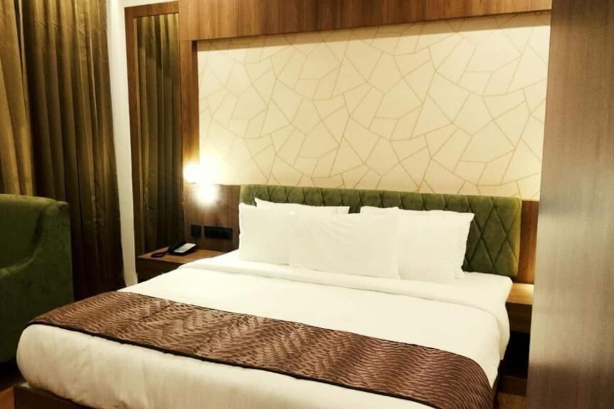A hotel room with a bed, a green armchair, a bedside table with a lamp, and a patterned headboard.