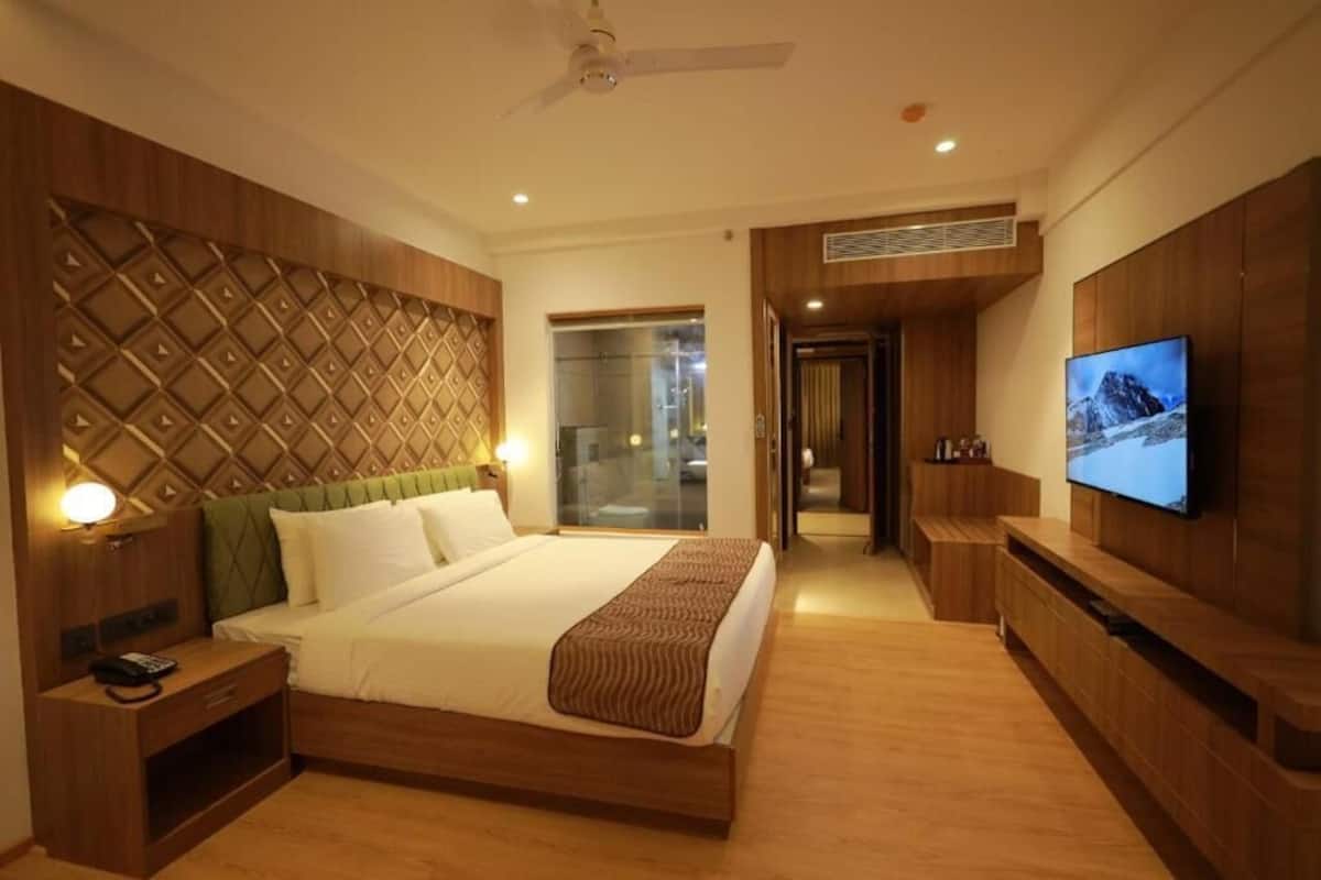 A hotel room with a bed, bedside table, TV, and a view of the outside.