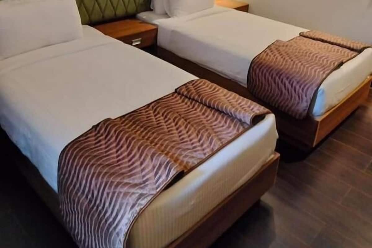 A hotel room with two beds, a green upholstered headboard, a patterned wall, and a nightstand with a lamp.
