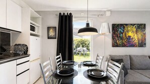 Cozinha moderna com armários brancos, uma mesa de jantar posta para quatro pessoas e um sofá cinza na sala de estar.