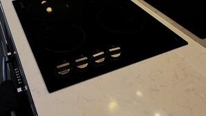 A kitchen with two black induction cooktops, a white countertop, and a stainless steel range hood. - Cozy Condo near Southern Cross / Pool & GYM (Melbourne)