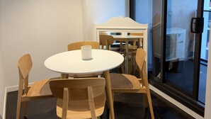 A modern dining area with a round table and wooden chairs, large windows, and a dark floor. - Cozy Condo near Southern Cross / Pool & GYM (Melbourne)