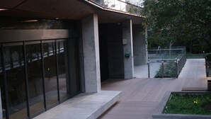 A modern building with large glass windows, a wooden deck, and a planter with greenery. - Cozy Condo near Southern Cross / Pool & GYM (Melbourne)