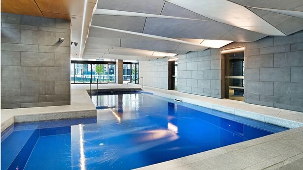 An indoor swimming pool with a clear view of the outside, surrounded by stone walls and a wooden ceiling. - Cozy Condo near Southern Cross / Pool & GYM (Melbourne)