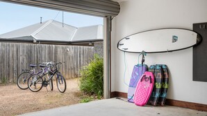 A garage with bicycles, a surfboard, and surfboards leaning against the wall. - Premium Location Family and Pet Friendly Property (Torquay)