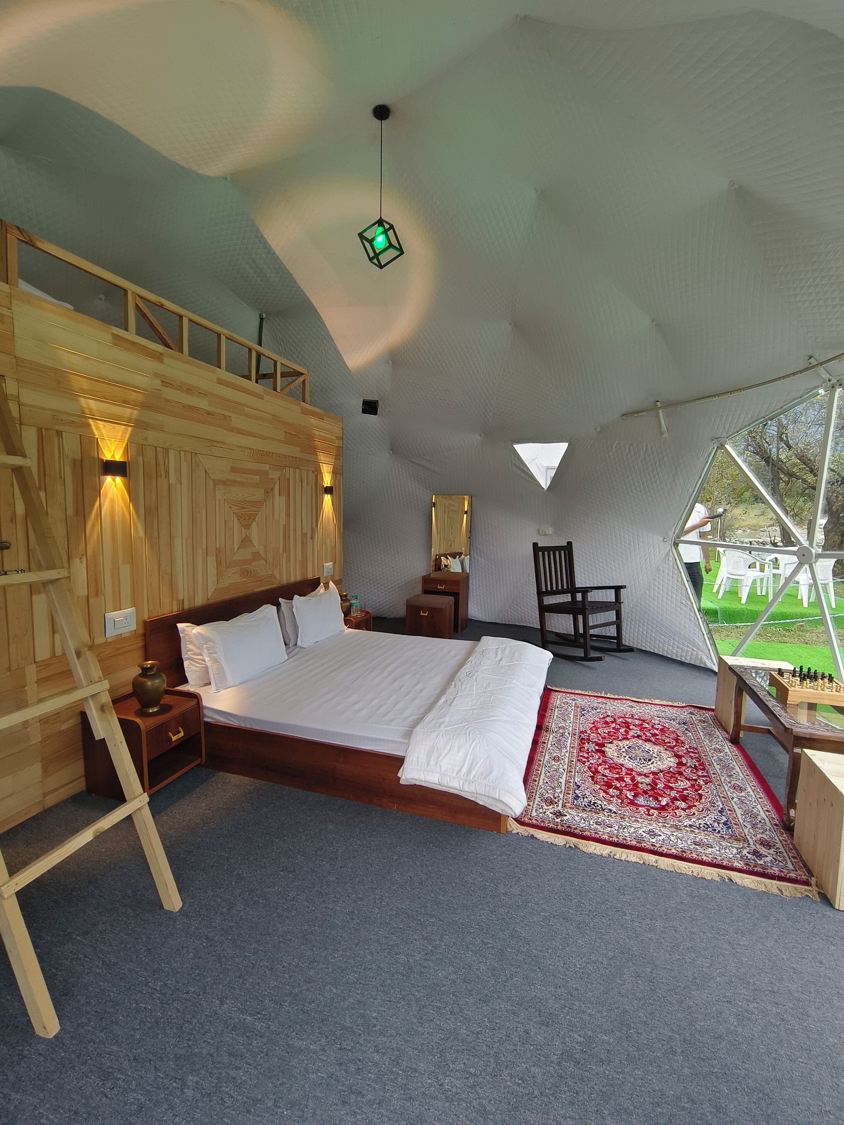 A cozy bedroom with a wooden bed, a red and white patterned rug, a small table, and a chair.