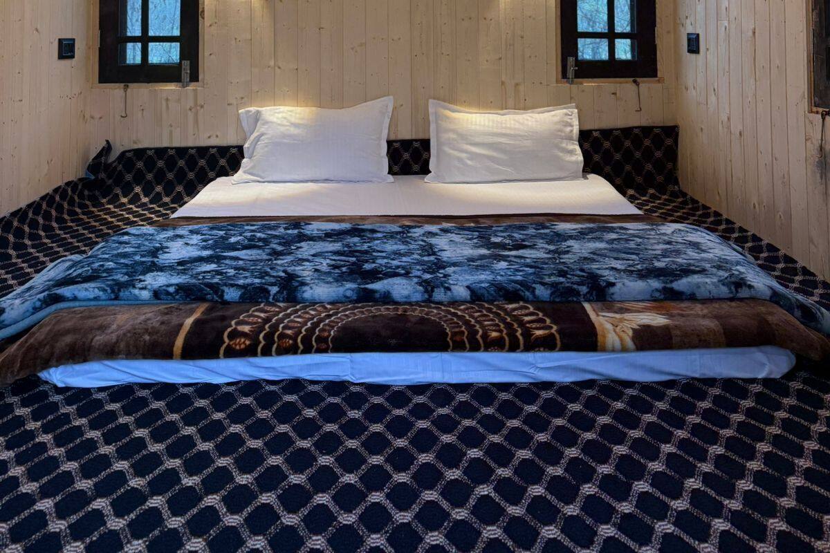 Quarto com paredes de madeira, uma cama com roupa de cama estampada, duas luminárias fixadas na parede e um lustre no teto.