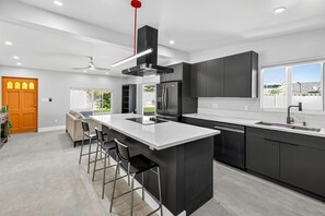 Eine moderne Küche mit einer zentralen Kochinsel, Barhocker, einem Kühlschrank und einem eingebauten Backofen.