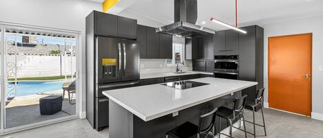 A modern kitchen with a central island, stainless steel appliances, and a view to an outdoor swimming pool.