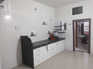 A kitchen with white cabinets, a black countertop, and a sink. - Shivvatsalya And Shivlaya Homestay (Nashik)