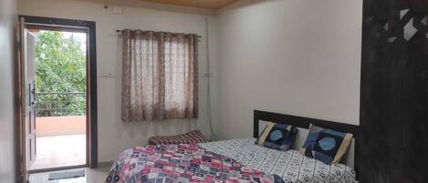 A bedroom with a bed, a ceiling fan, a window with curtains, and a balcony door.