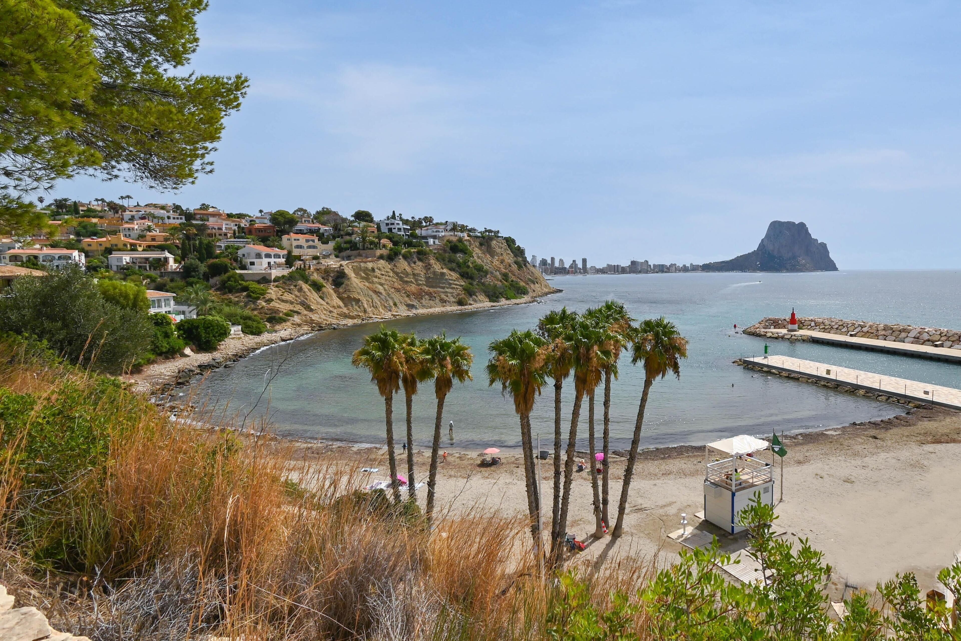 Eine Küstenstadt mit Strand, Palmen und einem Felsen im Hintergrund.
