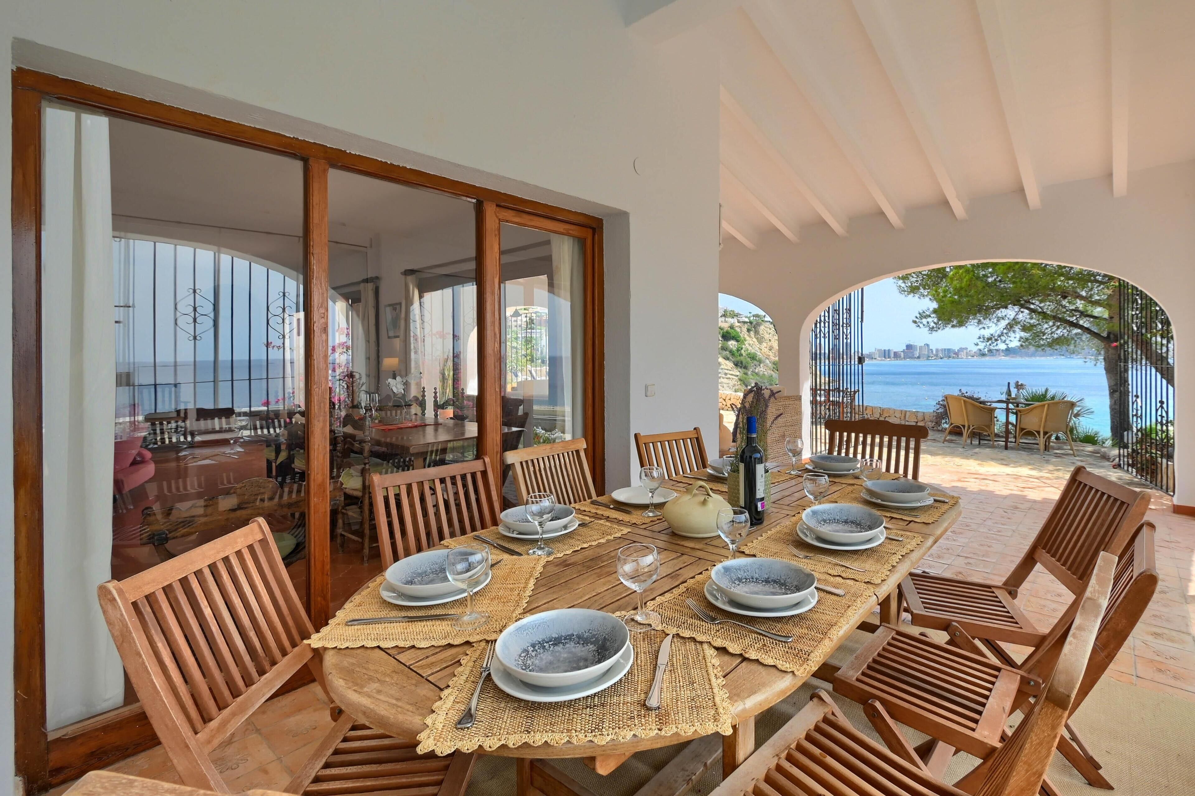 A dining area with a table set for six, wooden chairs, and a view of the sea.