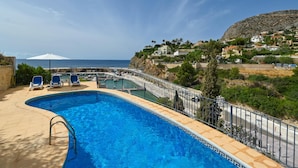 A swimming pool with a metal railing, blue chairs, and a white umbrella. - Casa Timeris 8 pax - Calpe, Costa Blanca (Calpe)