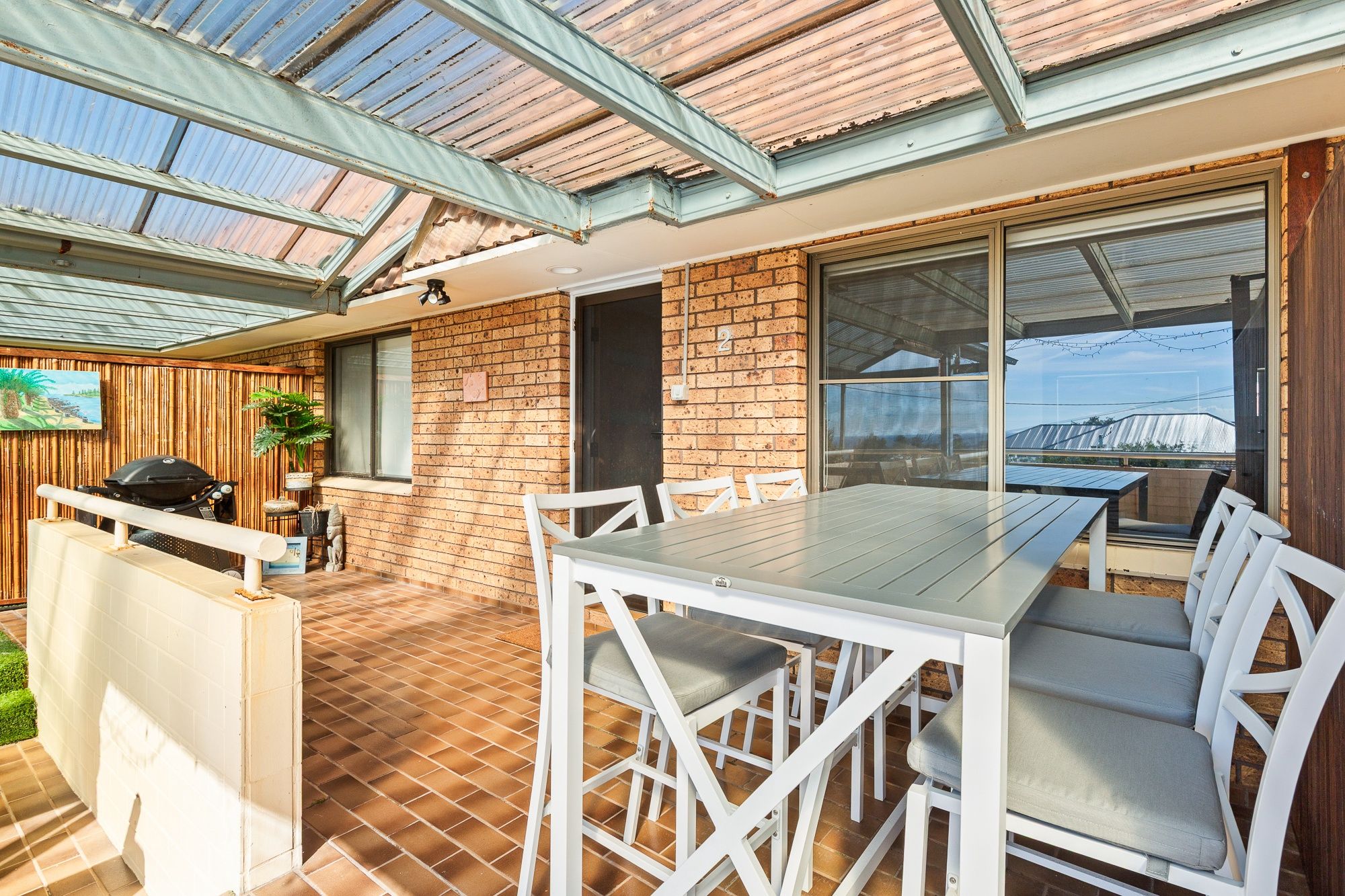 A covered patio area with a table and chairs, a grill, and a view of the surrounding landscape.