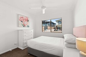 A bedroom with a bed, a dresser, a ceiling fan, a window with a view, and a painting.