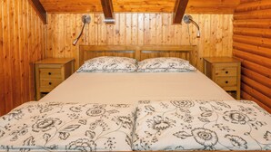 Quarto com painéis de madeira, uma cama, duas mesas de cabeceira e um lustre.
