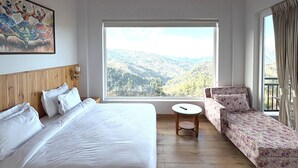 Ett sovrum med en stor säng, en soffa, ett litet bord, en tavla på väggen och utsikt över bergen.
