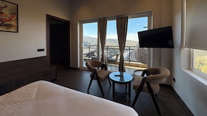 Ett hotellrum med en säng, två stolar, ett litet bord, en TV och en balkong med utsikt.
