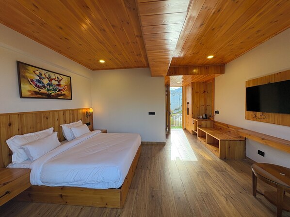 Una habitación con techo de madera, una cama con ropa de cama blanca, un cuadro en la pared y un televisor montado en la pared.