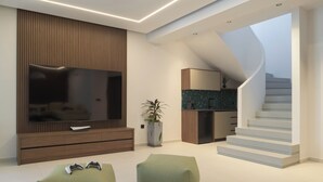 A modern living room with a flat-screen TV, wooden entertainment unit, green seating, and a staircase leading to an upper level. - Esse Villa, a Linear Sea-View Wellness Retreat (Maroulas)