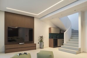 A modern living room with a flat-screen TV, wooden entertainment unit, green seating, and a staircase leading to an upper level. - Esse Villa, a Linear Sea-View Wellness Retreat (Maroulas)