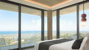 A bedroom with a large bed, a view of the sea, and a balcony with chairs. - Esse Villa, a Linear Sea-View Wellness Retreat (Maroulas)