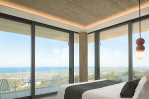 Ein Schlafzimmer mit einem großen Bett, Meerblick und einem Balkon mit Stühlen.