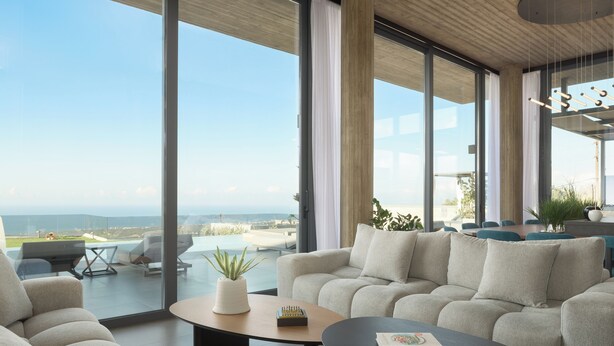 A modern living room with a large window, a sofa, a coffee table, and a view of the outdoors. - Esse Villa, a Linear Sea-View Wellness Retreat (Maroulas)