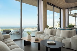Ein modernes Wohnzimmer mit großem Fenster, einer Couch, einem Couchtisch und Blick ins Freie.