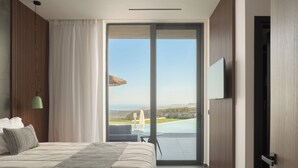 A modern hotel room with a large bed, a view of a pool and landscape, and a sliding glass door to the outdoors. - Esse Villa, a Linear Sea-View Wellness Retreat (Maroulas)