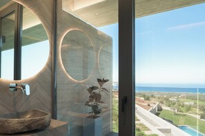 Ein modernes Badezimmer mit einem großen Spiegel, einem Waschbecken und Blick auf den Ozean.