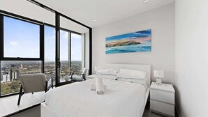 Moderni hotellihuone, jossa on suuri sänky, työpöytä, tuoli, yöpöytä ja maalaus, jossa on kuvattuna merimaisema.
