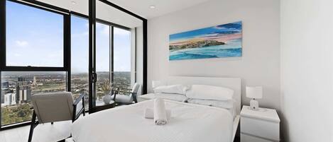 Een moderne hotelkamer met een groot bed, een bureau, een stoel, een nachtkastje en een schilderij van een kustlandschap.