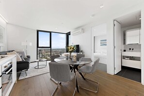 A modern living room with a dining area, large windows, and a city view. - City-View 1-Bed Retreat Near Queen Vic (Melbourne)
