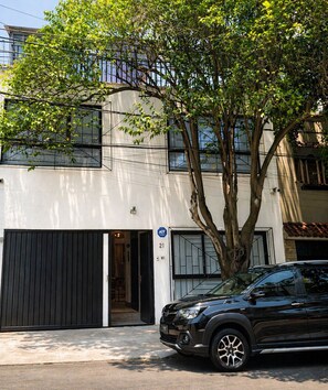 A modern building with a black car parked in front, a tree in the foreground, and a clear sky. - Full house in Condesa, 4 bedrooms, terrace and 3 levels (Ciudad de México)