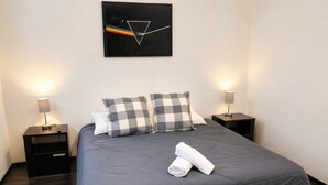 A neatly made bed with a grey duvet, two checkered pillows, and a rolled white towel. There are two bedside tables with lamps, and a black artwork with a triangle and rainbow on the wall. - Full house in Condesa, 4 bedrooms, terrace and 3 levels (Ciudad de México)