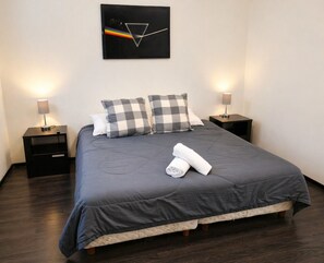 A neatly made bed with a grey duvet, two checkered pillows, and a rolled white towel. There are two bedside tables with lamps, and a black artwork with a triangle and rainbow on the wall. - Full house in Condesa, 4 bedrooms, terrace and 3 levels (Ciudad de México)